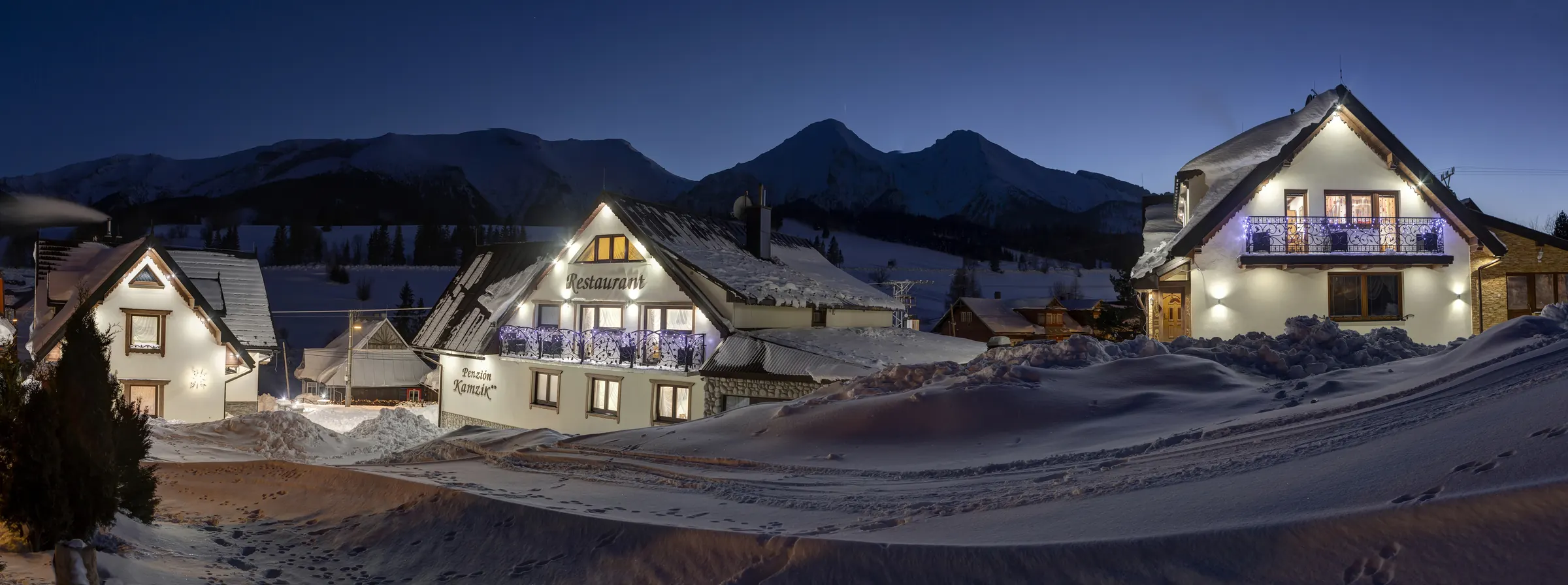 Penzión Kamzík v zimnej noci, za ním zasnežené Belianske Tatry