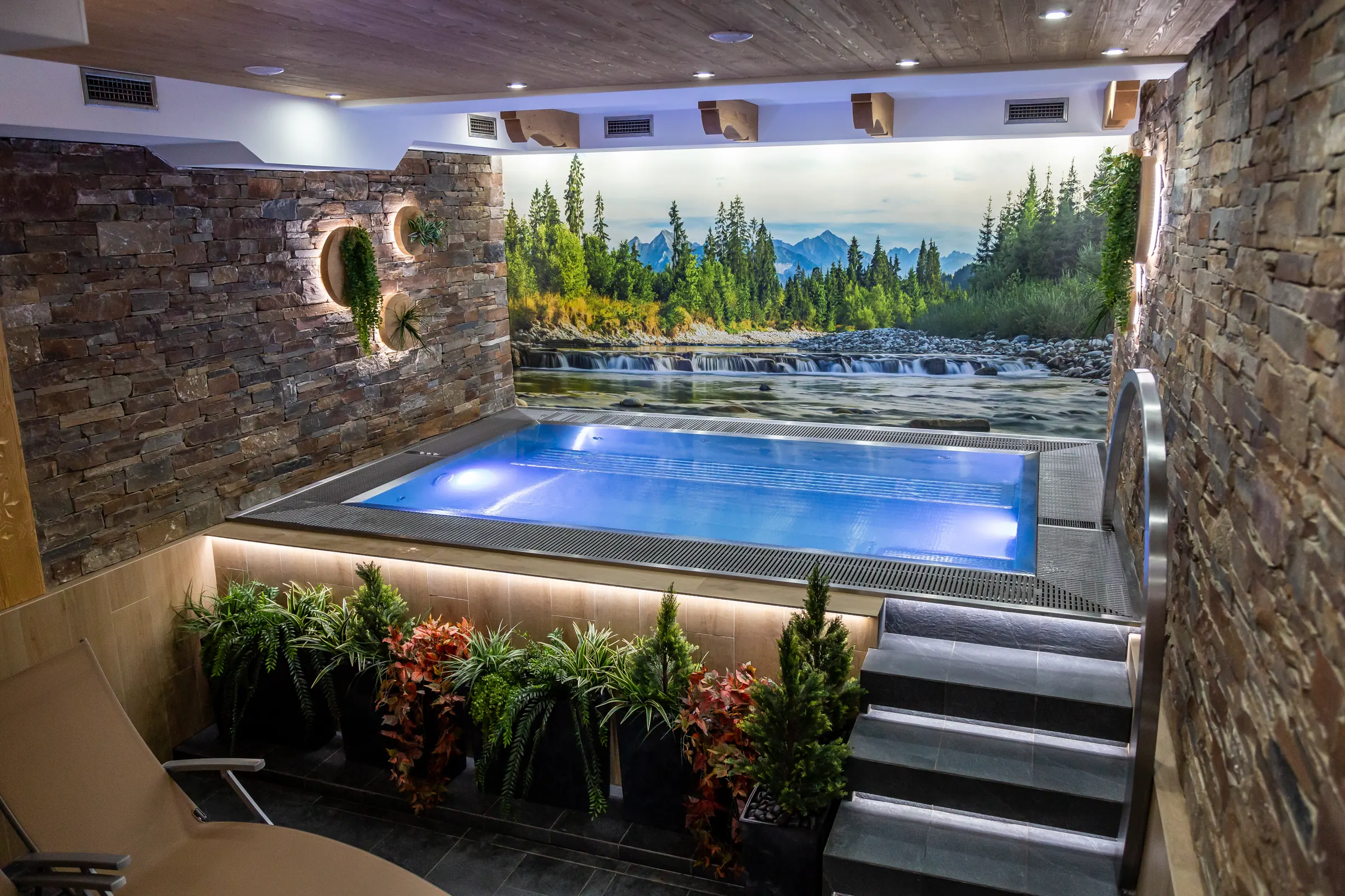 Vírivý bazén wellness Resortu Kamzík s kamennou stenou, maľbou horského jazera a zeleňou